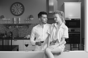 Young caucasian couple sitting at home ktichen, hugging, smiling, drinking red wine. Young lovers having good time. Blonde woman and brunette man