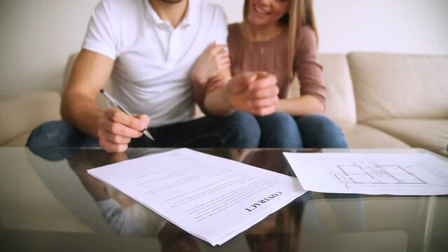 Happy married couple signing contract of sale purchase, hugging, satisfied young clients putting signature on mortgage loan agreement, buying renting real estate, making property investment. Close up