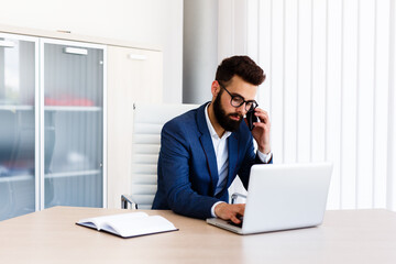 Obraz premium Businessman on his work place using laptop and phone to communicate with others