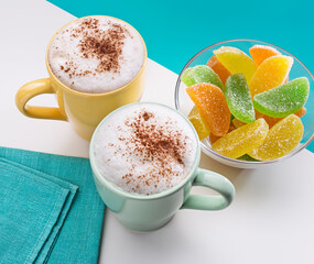 Two cups of cappuccino with cinnamon and jelly sweets.