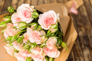 Bouquet of pink blooming fresh roses with buds n wrap on wooden table