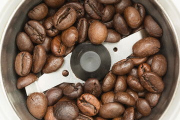 Fried dark coffee beans in an automatic coffee grinder, close-up food background