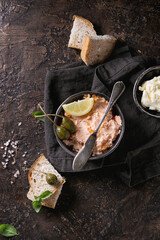 Black bowl of salmon pate with red caviar served with butter, sliced bread, capers, vintage knife...