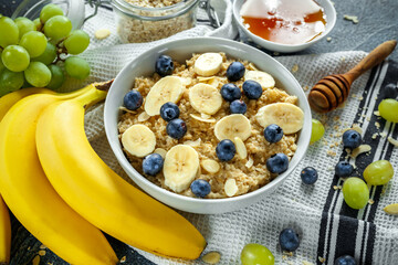Bowl of Healthy Breakfast oatmeal with ripe blueberries, banana, honey, almonds and green grape. Top view