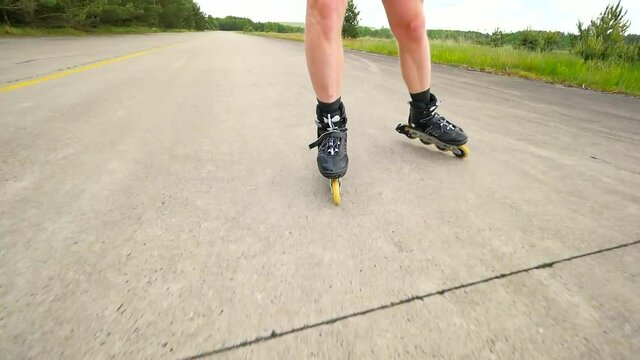 Shuffle inline skating on way in pine forest. Mans legs roller skating on the asphalt in hot summer day. Close up view to quick shuffle movement of four wheels inline boots.