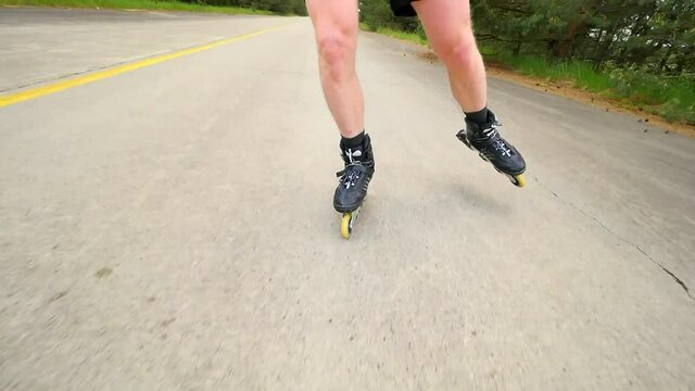 Easy shuffling inline skating on way with painted yellow line. Mans legs roller skating on the asphalt in hot summer day. Close up view to quick shuffle movement of four wheels inline boots.