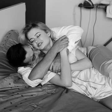 Young romantic couple relaxing and hugging in bed. Pretty beautiful blonde girl and brunette man. Black and white photo.