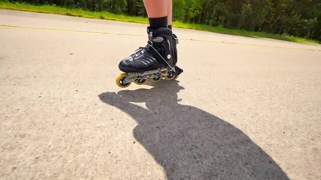 Very close up side view to working inline skates. Easy skating on the smooth  asphalt. Close up view to quick movement of black four wheels inline boots.