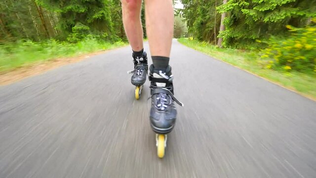 Shuffle skating and braking with t-style brake in park. Mans legs roller skating on the asphalt in hot summer day. Close up view to quick shuffle movement of four wheels inline boots.
