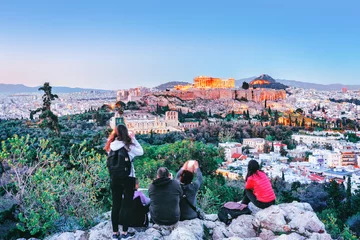 Fotobehang Mensen in Athene die bezienswaardigheden bezoeken in het oude gebouw van de Akropolis vanaf de heuvel Filosofie, zonsonderganglandschap Griekenland. © Feel good studio