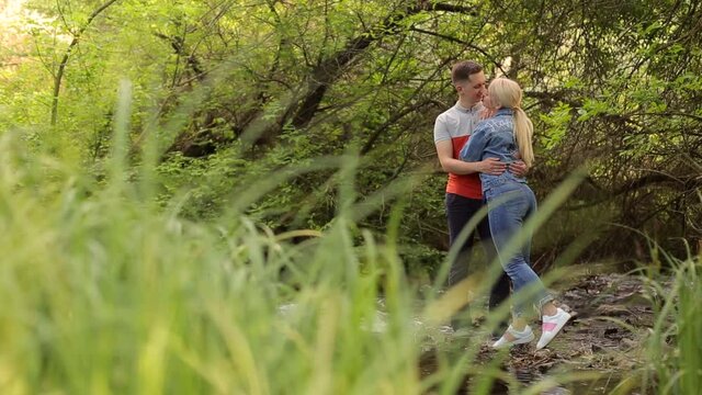 Loving couple hugs and kisses standing on the rocks in a shallow river in the wild. Young couple standing in embrace in the middle of forest river.