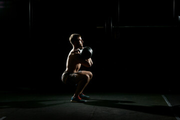 Fitness training. Man doing sit ups with weights in dark gym.