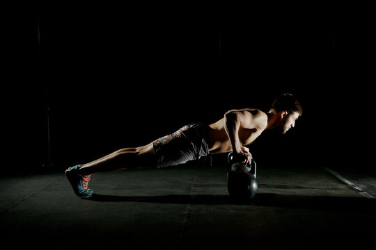 Fitness training. Man doing push ups exercise using dumbbells or weights in dark gym.