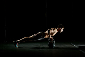 Fitness training. Man doing push ups exercise using dumbbells or weights in dark gym.