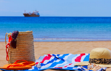 beach towel and sunbathing accessories on sandy beach by the bleu sea waters and ship