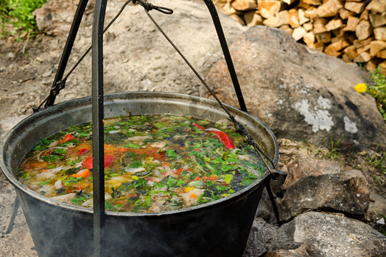 A pot of soup is hung over the fire. In the background there are firewood.