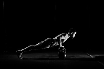 Fitness training. Man doing push ups exercise using dumbbells or weights in dark gym.