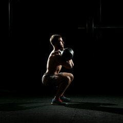 Fototapeta na wymiar Fitness training. Man doing sit ups with weights in dark gym.