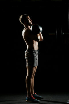 Fitness training. Man doing exercises with weights in dark gym.
