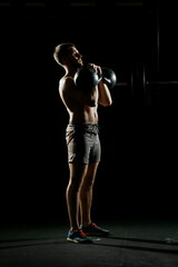 Fitness training. Man doing exercises with weights in dark gym.
