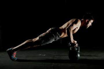 Fitness training. Man doing push ups exercise using dumbbells or weights in dark gym.