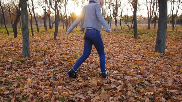 Young woman happiness dancing among the autumn colorful leaves in sunset