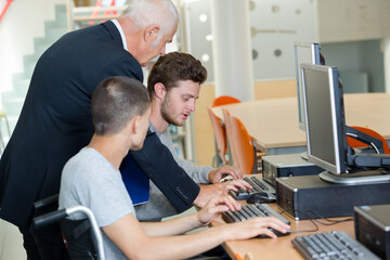 Teacher helping young men using computers, one in wheelchair