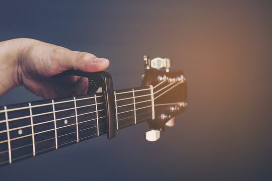 Vintage color picture of man putting guitar capo over gray background
