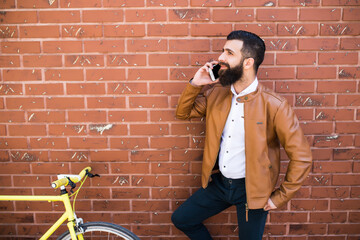 Fototapeta na wymiar Young hipster man speak phone with his fixed bicycle on the wall