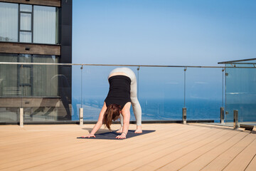 sport woman doing stretching yoga exercise on hotel roof with wooden floor stand on yoga mat