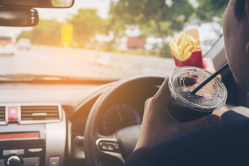 Man driving car while eating French fries and soft drink, left-driving countries