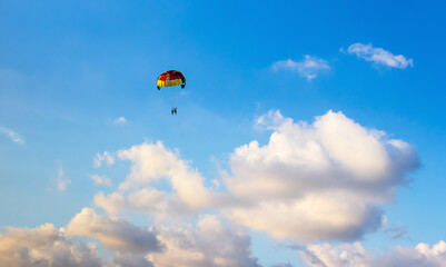multicolored parachute floats high in the sky among the clouds in the light of the setting sun parasailing