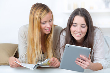 Two teenage girls, one with a magazine the other with a tablet