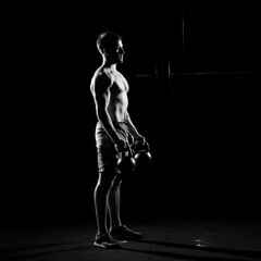 Fototapeta na wymiar Fitness training. Man doing exercises with weights in dark gym.