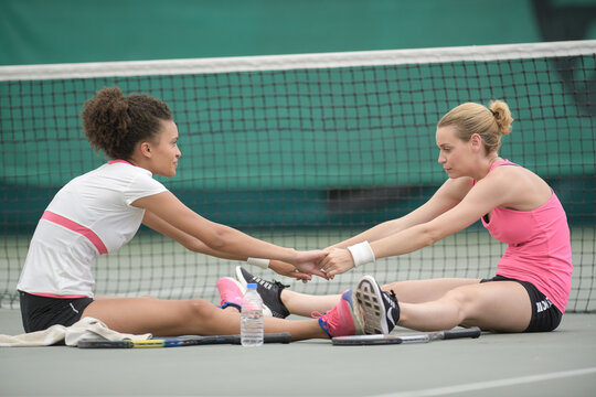 Women on tennis court stretching together