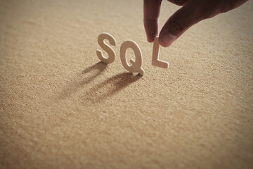 SQL wood word on compressed board with human's finger at L letter