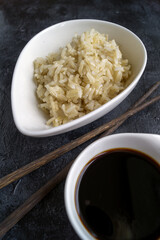 Japanese sushi with chopsticks over a bowl of soy sauce, brown rice and chukka salad on a black background. Top view with copy space.