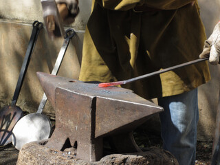 Blacksmith manually forging the molten metal with hammer on the anvil
