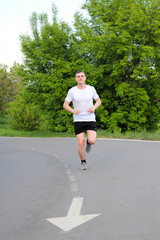 молодой спортсмен бежит по беговой асфальтированной дорожке в парке летом