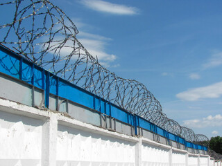 Barbed wire on the wall against the blue sky