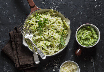 Vegetarian pasta farfalle with broccoli pesto in a cast iron skillet on the dark table, top view