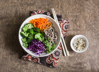 Broccoli, buckwheat noodles, red cabbage and pickled carrots buddha bowl on wooden background, top view. Vegetarian healthy diet food concept