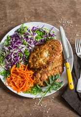 Chicken schnitzel tempura, red and white cabbage coleslaw and spicy pickled carrots on a wooden background, top view. Delicious lunch