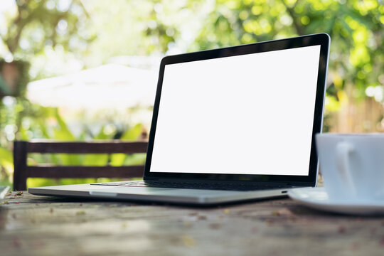 Mockup image of laptop with blank white screen and coffee cup on vintage wooden table in nature outdoor park