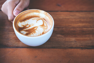 A hand holding a cup of hot coffee on wooden table in vintage cafe