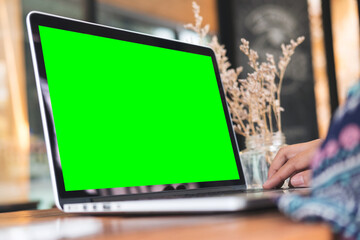 Mockup image of a woman using laptop with blank green screen on wooden table in office