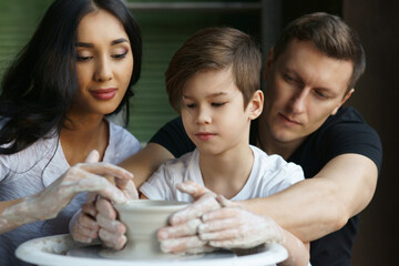 Family working on pottery wheel. Mother and father teaching their son to scupl or make clay pot