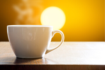 Cup of coffee on wooden table in sunrise