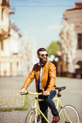 Confident young bearded man in sunglasses riding on his bicycle along the sunny street