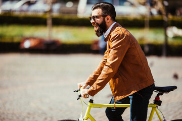 Obraz premium Young bearded man riding on his bicycle outdoors on sunny street